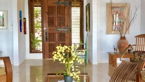 A spacious room with a wooden ceiling, a large wooden door, a chandelier, and a dining table with a potted plant. - Zandoli Villa
Simply Awesome Views (Cap Estate)