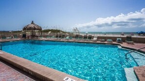 A swimming pool with lounge chairs and a gazebo, surrounded by a fence and a beach view.