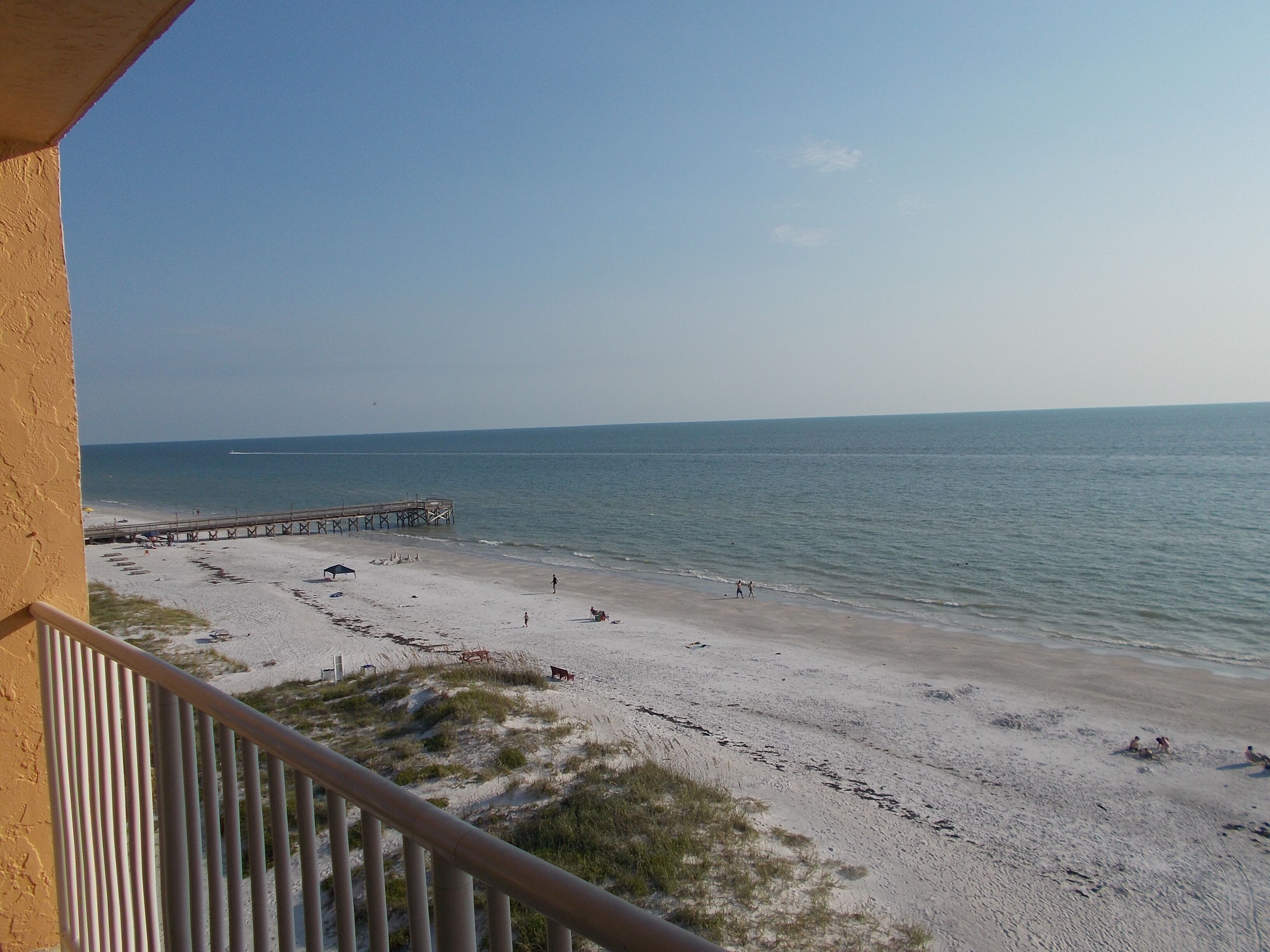A beach with a pier extending into the water, sandy beach, and a clear sky.