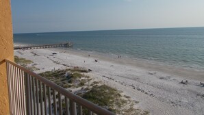 A beach with a pier extending into the water, sandy beach, and a clear sky.