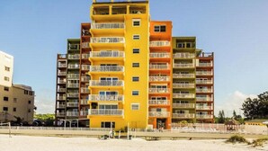 A multi-story hotel with balconies, located near a beach.