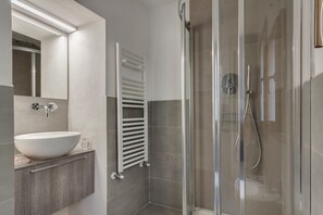 Een moderne badkamer met een groot wit wastafel, een douche met glazen wanden en een handdoekrek.
