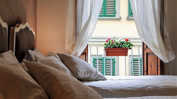 A bedroom with a bed, white curtains, and a view of a balcony with a flower pot. - UFFIZI-PONTE VECCHIO- Extraordinary Location- Wonderful Apartment-elevator (Firenze)