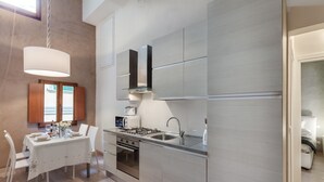 A modern kitchen with a dining area, featuring stainless steel appliances, a glass-top table, and wooden cabinets. - UFFIZI-PONTE VECCHIO- Extraordinary Location- Wonderful Apartment-elevator (Firenze)