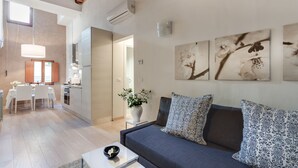 A modern living room with a sofa, a coffee table, and a dining area with a table and chairs. There are wall-mounted air conditioning units and a large window providing natural light. - UFFIZI-PONTE VECCHIO- Extraordinary Location- Wonderful Apartment-elevator (Firenze)