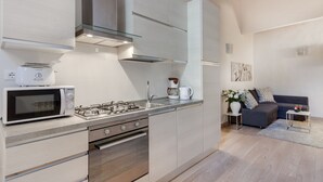 A modern kitchen with a built-in microwave, gas stove, and oven. There is a coffee maker and a sink. The kitchen is adjacent to a living area with a sofa and a small table. - UFFIZI-PONTE VECCHIO- Extraordinary Location- Wonderful Apartment-elevator (Firenze)