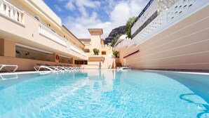 A pool with clear blue water, surrounded by beige buildings with balconies and a mountain in the background. - APARTMENT A few meters from a black sand beach. (Santiago del Teide)