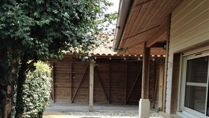 Ein Holzgebäude mit überdachter Terrasse, umgeben von einer Hecke und einem Holzspanschichtbett.