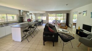 Eine moderne Küche mit Kochinsel, Essbereich mit Stühlen, einer Couch und einem Fernseher.