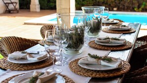 A dining table set with glassware, plates, and woven placemats, overlooking a pool. - Villa Sa Coma - A Perfect Retreat for Your Dream Vacation! (Cala Millor)