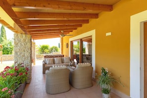 Un patio cubierto con mobiliario de mimbre, pilares de piedra y vistas al exterior.