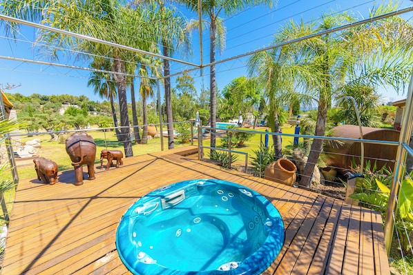 A wooden deck with a hot tub, surrounded by palm trees and a pool.