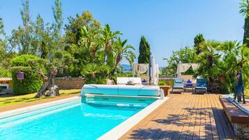 A swimming pool with a wooden deck, lounge chairs, and tropical vegetation.