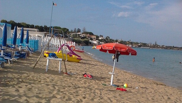 Ein Strand mit Sand, Sonnenschirmen und Liegestühlen.