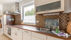 A modern kitchen with a wooden countertop, stainless steel sink, and a window with a view of greenery.