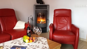 A living room with two red leather chairs, a table with a fruit bowl and wine bottle, and a wood-burning stove.