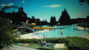 Ein Poolbereich mit Volleyballplatz, umgeben von Bäumen und einer überdachten Sitzgelegenheit.
