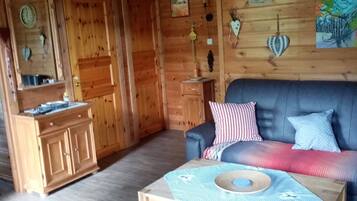 Ein gemütliches Blockhaus-Interieur mit Holzboden, einer Couch mit gemusterten Kissen, einem Holztisch und einer Pendelleuchte.