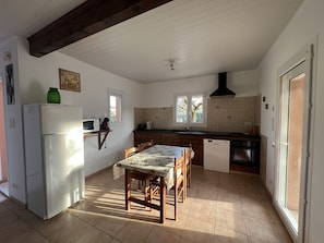 Una cocina con una mesa de comedor, sillas, refrigerador, microondas, fregadero y ventana.