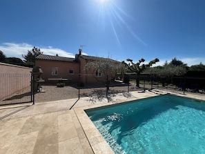 Una piscina con borde de baldosas, una casa con tejado de cerámica y un cielo azul despejado.