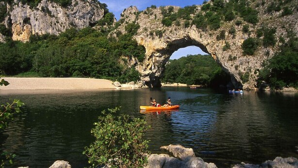 A natural rock arch over a calm river with kayaks.