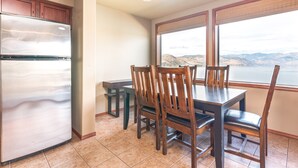 A kitchen with a stainless steel refrigerator, wooden cabinets, a dining table with chairs, and a view of mountains through large windows. - GrandView 402 - 2 Bedroom Waterfront Condo (Chelan)