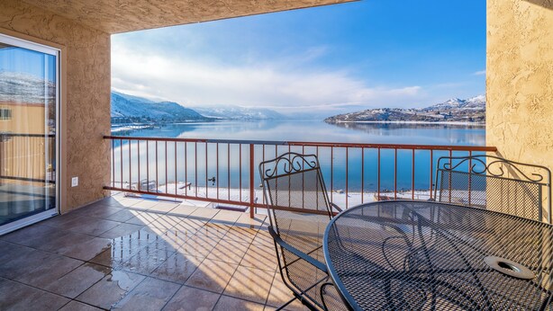 A balcony with a metal table and chairs, overlooking a calm lake and snow-capped mountains. - GrandView 402 - 2 Bedroom Waterfront Condo (Chelan)