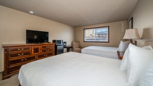 Een hotelkamer met twee bedden, een televisie, een bureau met computer, een stoel en een raam met zonwering.