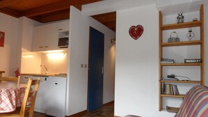 A cozy living room with a wooden floor, a plaid sofa, a bookshelf, and a blue door leading to a kitchen. - At the base of the slopes, apartment with balcony/terrace, enclosed garage, nearby shops (Beaufort)