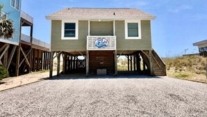 Una casa frente a la playa con un letrero Stay Sandy, terraza de madera y camino de entrada de grava.