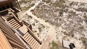Una playa con una terraza de madera, sombrillas y un sendero arenoso que lleva al agua.