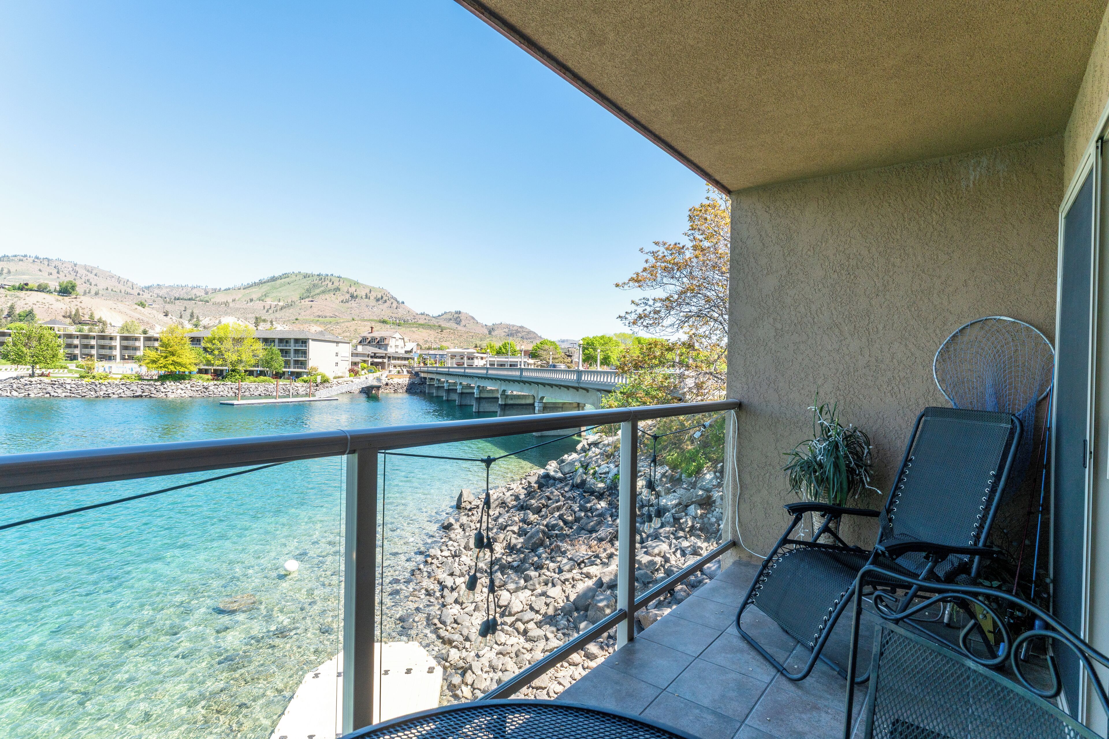 Un balcon offrant une vue dégagée sur une rivière et des collines lointaines, avec une chaise et une petite table.