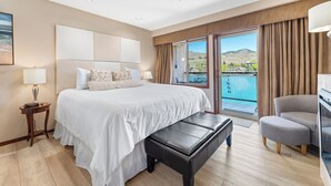 A hotel room with a large bed, a bench, a chair, a nightstand, and a view of a body of water through the window. - Grandview #722 Waterfront King Suite River View (Chelan)