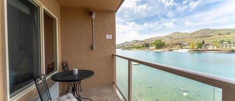 Ein Balkon mit Tisch und Stühlen, mit Blick auf einen See und Hügeln sowie Gebäude in der Ferne.