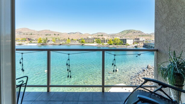 A balcony with a clear view of a lake, mountains, and buildings in the background. - Grandview #722 Waterfront King Suite River View (Chelan)