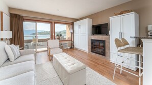 A modern living room with a sofa, ottoman, and a high chair. There is a fireplace and a television. The room has large windows with a view of the outdoors. - Grandview 511 - Waterfront (Chelan)