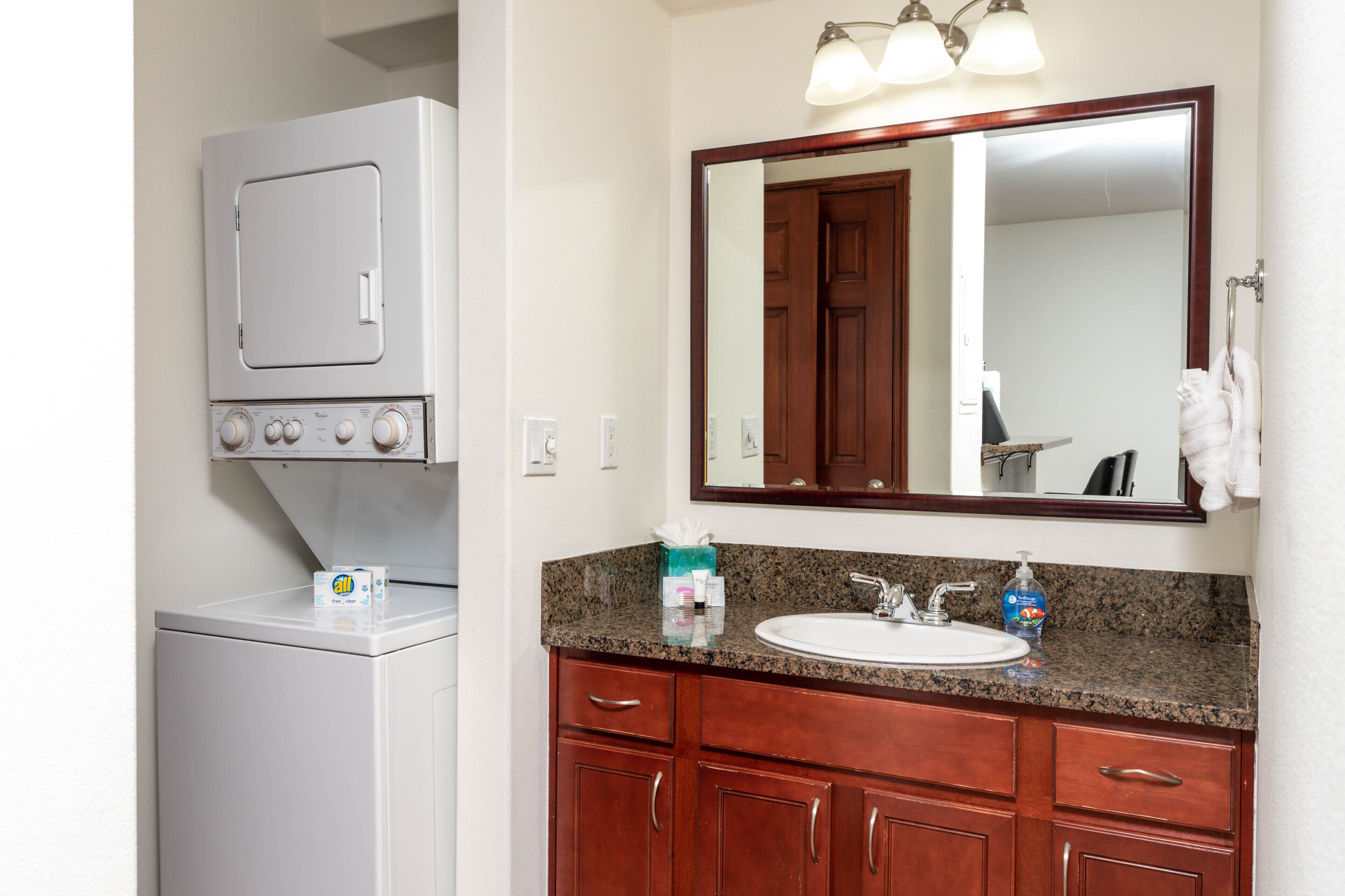 A bathroom with a white washing machine, a sink with a granite countertop, and wooden cabinets.