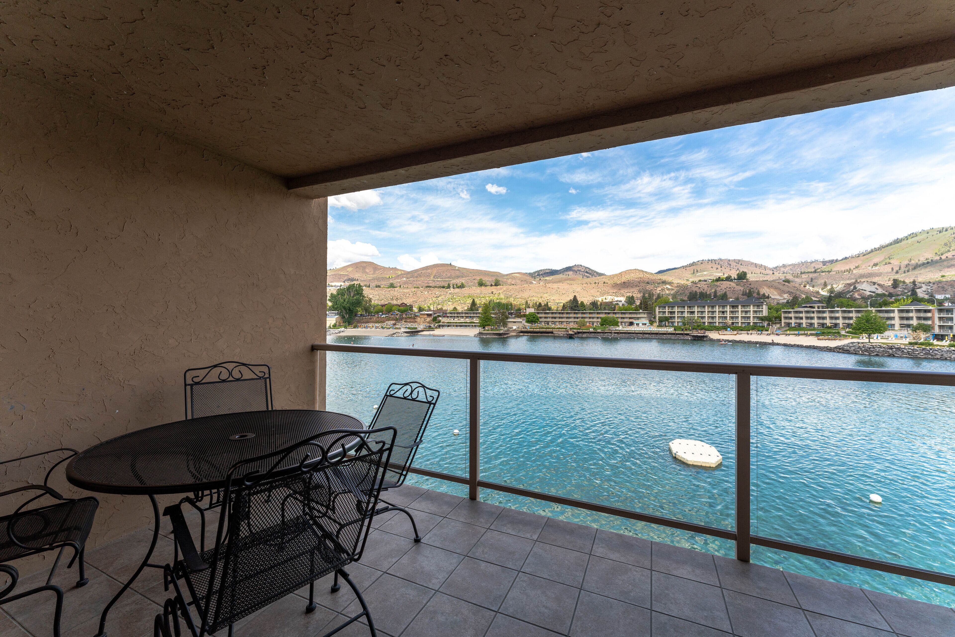 A balcony with a table and chairs overlooking a body of water and distant hills.