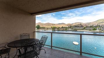 A balcony with a table and chairs overlooking a body of water and distant hills.