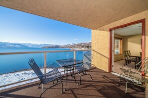 Un balcón con una mesa y sillas, con vista a un lago y montañas al fondo.