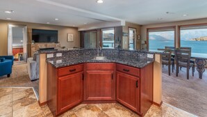 A modern kitchen with granite countertops, wooden cabinets, and a large island. It features a view of the sea through large windows. - Grandview 532 Executive Waterfront condo (Chelan)