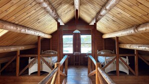 A cabin with a high ceiling, wooden beams, a central staircase, and a window with a view of the outdoors. - Waterfront Log Home on Quiet Lake - 25 Minutes -Sunday River Ski (Waterford)