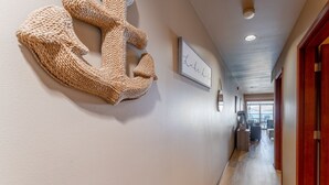 En hall med ett väggkonstverk i form av en stickad tavla, en inramad skylt och ett trägolv som leder till en sittgrupp med utsikt.