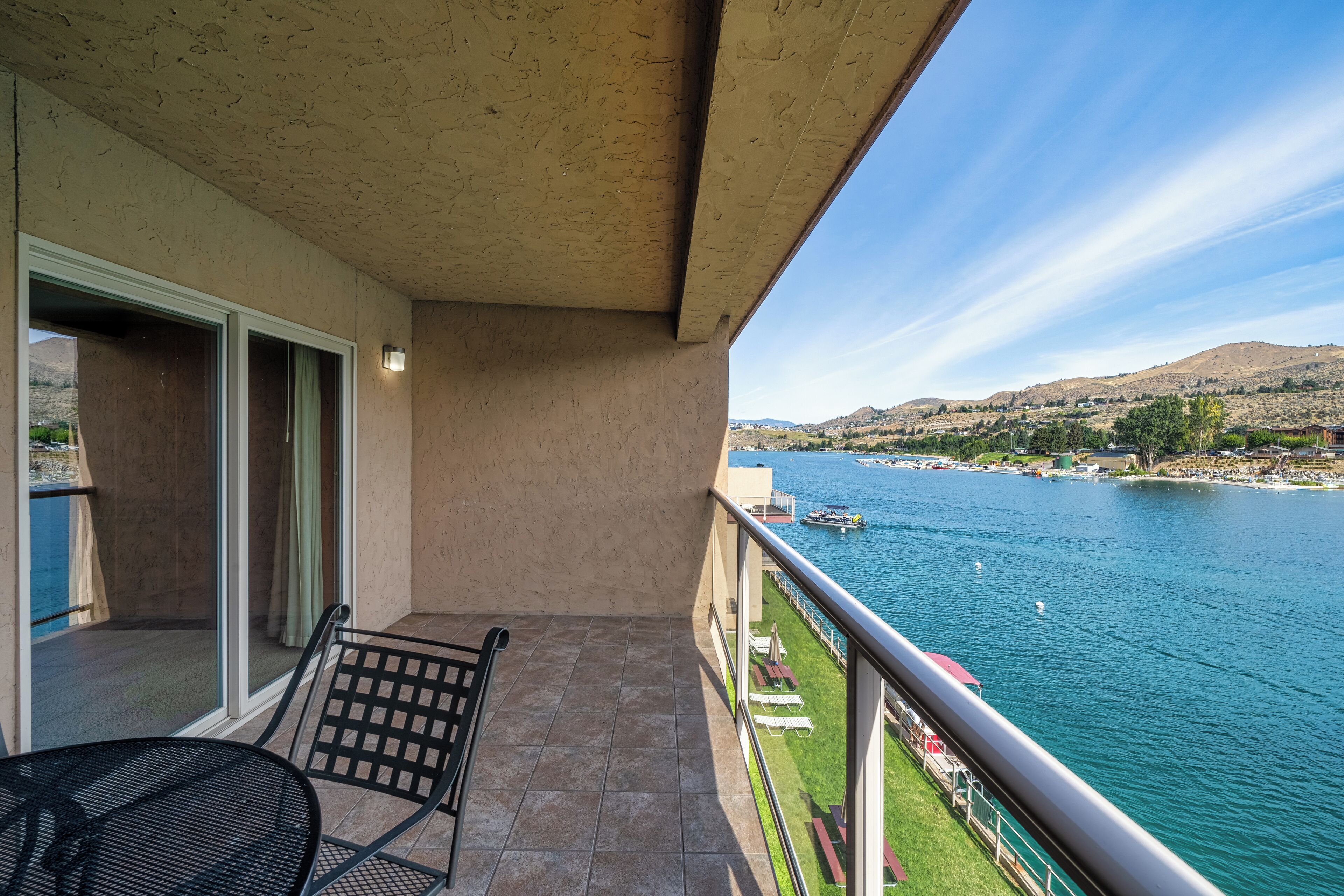 A balcony with a view of a river, a chair, and a table.