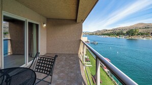 A balcony with a view of a river, a chair, and a table.