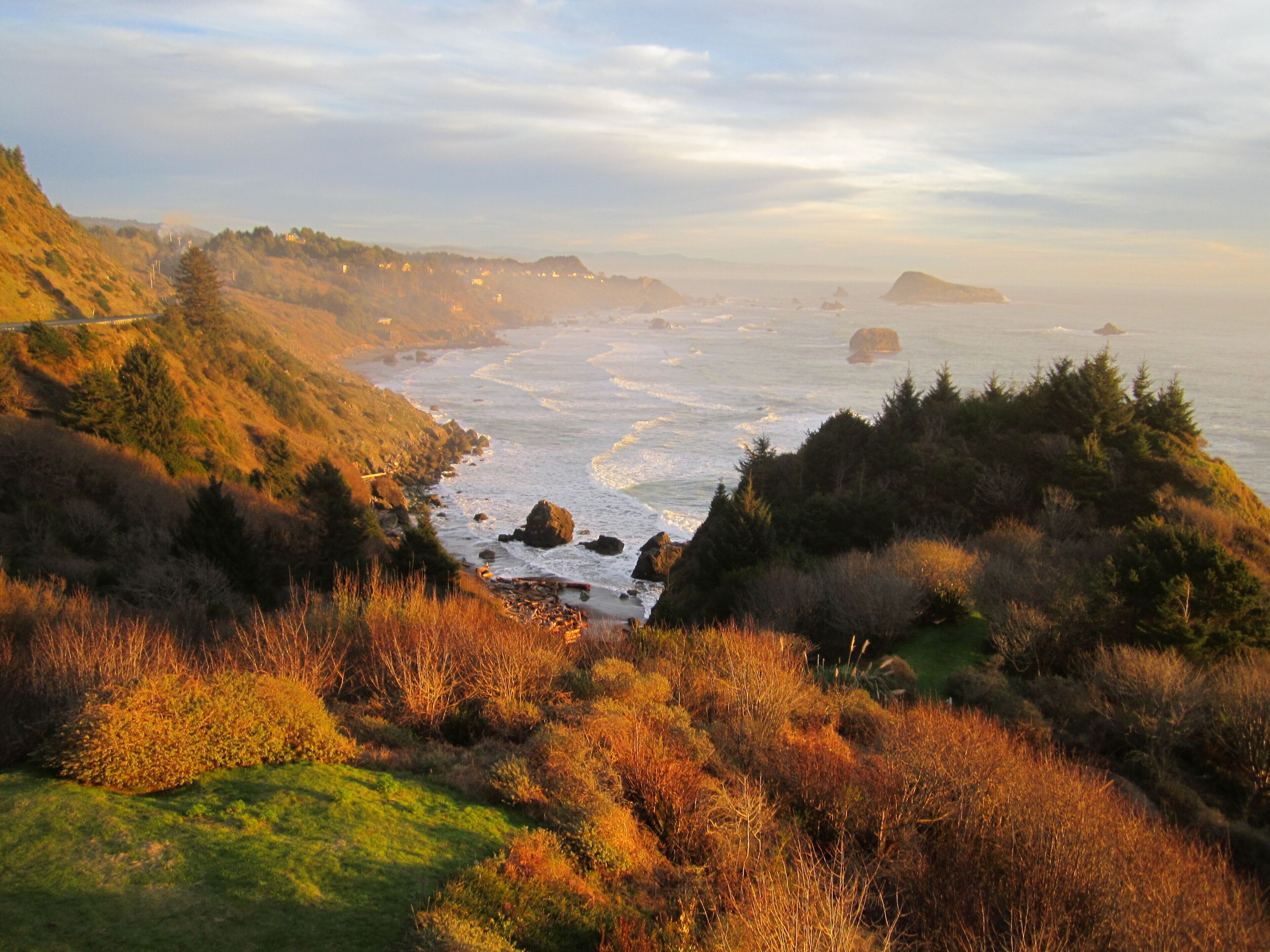 A coastal landscape with a view of the ocean, rocky shoreline, and hills.