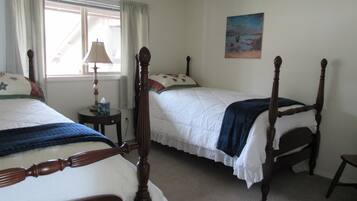 A bedroom with two single beds, a bedside table with a lamp, a painting on the wall, and a window with curtains.