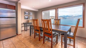 A dining area with a large table and chairs, a refrigerator, and a view of a lake and mountains through a large window. - GrandView 304 - 2 Bedroom Waterfront Condo (Chelan)