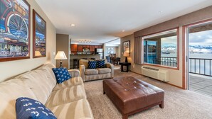 A spacious living area with a sofa, ottoman, and a view of a balcony with a scenic landscape. - GrandView 304 - 2 Bedroom Waterfront Condo (Chelan)