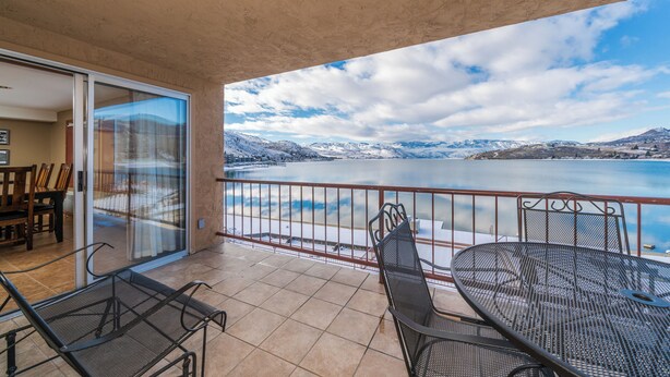 A balcony with a table and chairs, a view of a lake, and a mountainous landscape. - GrandView 304 - 2 Bedroom Waterfront Condo (Chelan)